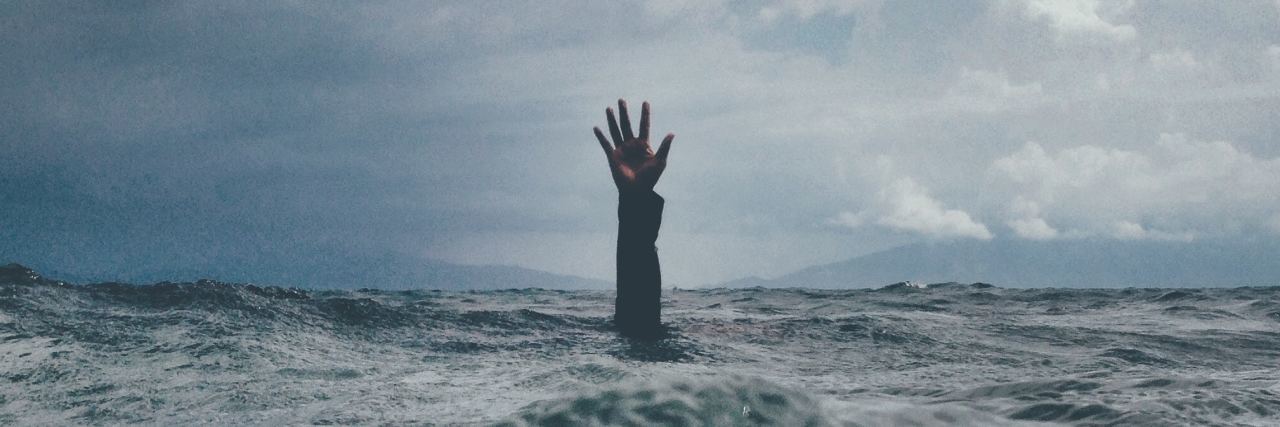 photo of hand reaching from ocean against backdrop of stormy skies