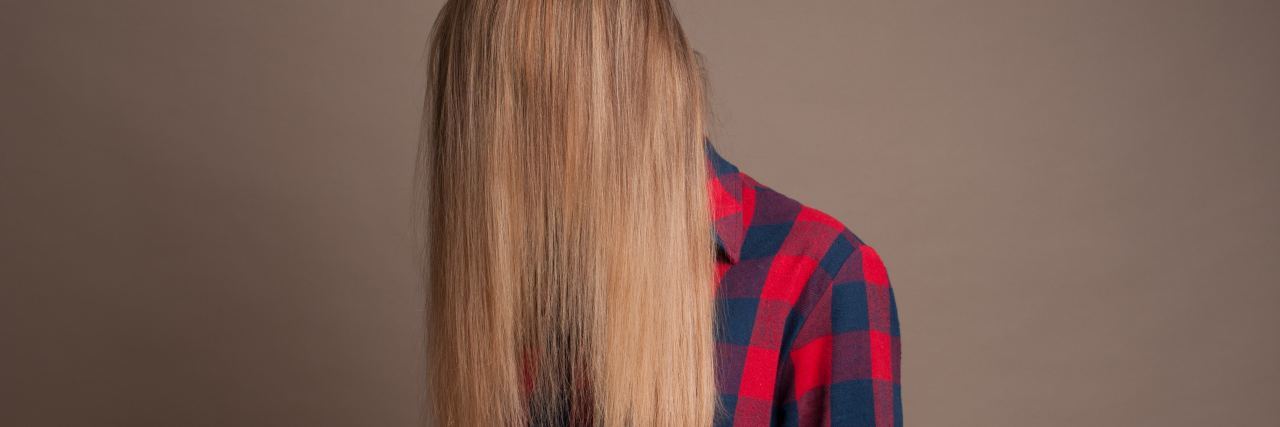 photo of blonde woman against plain background, wearing checkered red shirt and with hair covering face