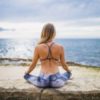 photo of woman in fitness clothes sitting by ocean cross-legged