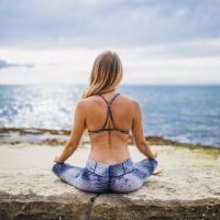 photo of woman in fitness clothes sitting by ocean cross-legged