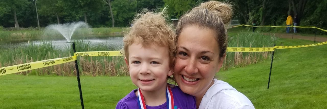 When My Daughter With Cerebral Palsy Ran Her First Race Mother hugging daughter, both smiling at a camera. Faughter wears a medal around her neck for finishing her race.