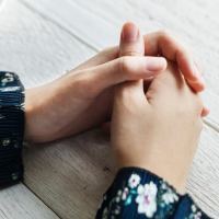 close up photo of woman's hands on table clasped beside cup of tea