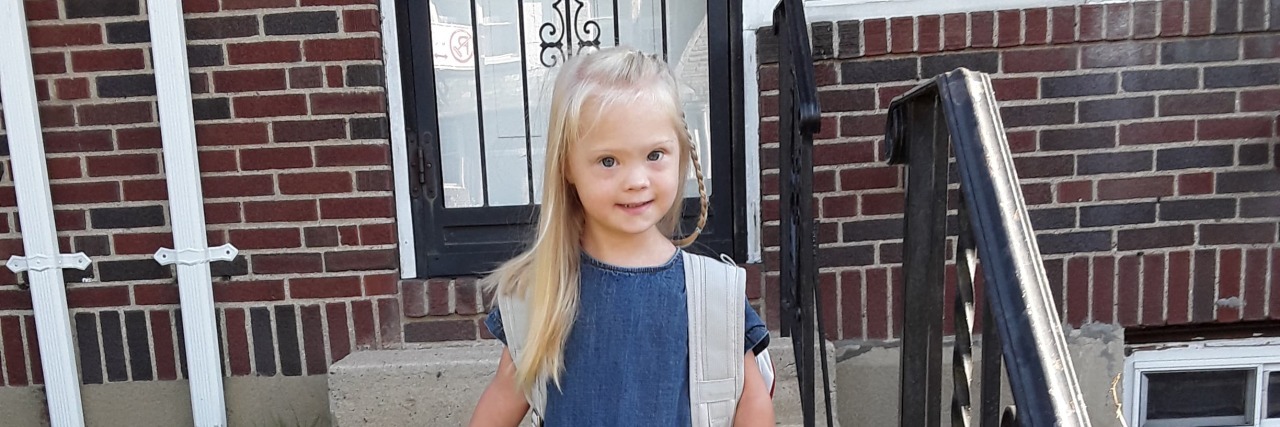 How to Read Your Child's Progress Report Without Freaking Out Little girl with Down syndrome standing utside her house with her backpack on