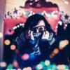 photo of woman wearing glasses covering part of face with scarf while surrounded by lights