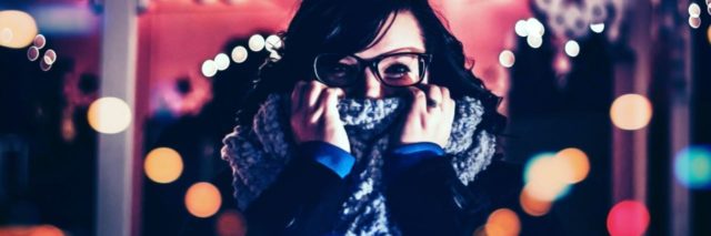 photo of woman wearing glasses covering part of face with scarf while surrounded by lights