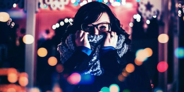 photo of woman wearing glasses covering part of face with scarf while surrounded by lights