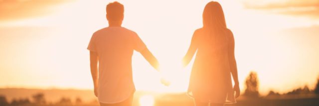 photo of couple standing hand in hand watching sunset together
