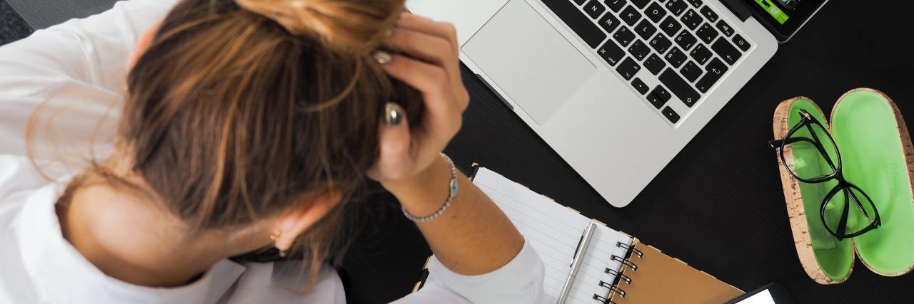 Self-Care When You Can’t Keep Working woman sitting on bed with laptop looking frustrated overhead view