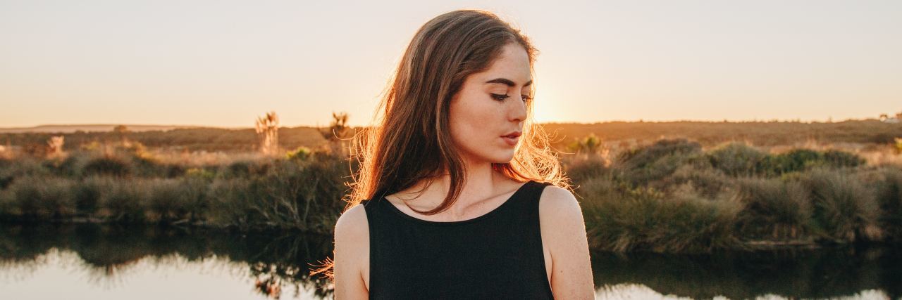 Common Signs of Anxiety We Often Don't Notice photo of woman standing in front of lake or pond at sunset
