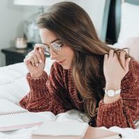 photo of woman lying on bed with glasses and notepads