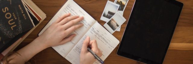 close up overhead photo of woman writing in diary or journal with coffee, glasses, notebook and laptop on wooden desk