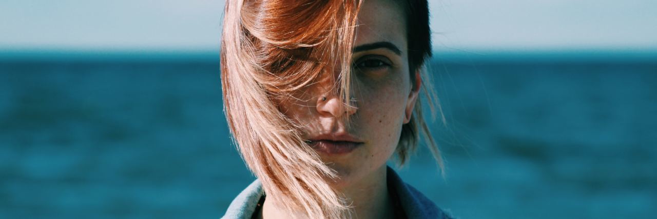 My High School Teacher Said My Anxiety Was an Excuse young woman with sea behind her looking into camera serious