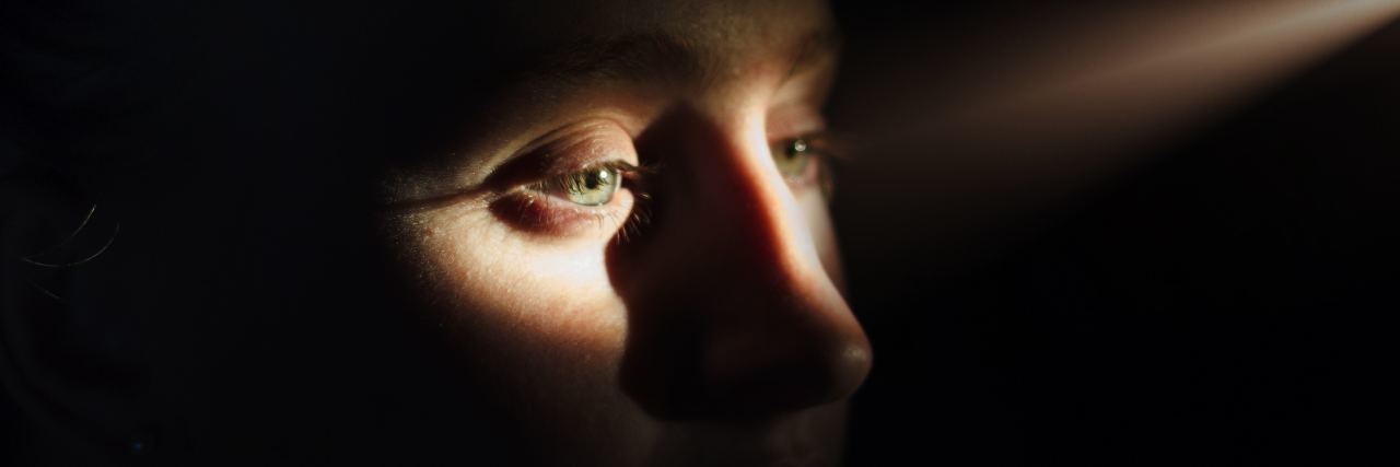 What Depression Looks and Feels Like woman standing in a dark room with a single ray of light shining in and illuminating her eyes