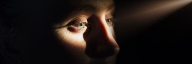 woman standing in a dark room with a single ray of light shining in and illuminating her eyes