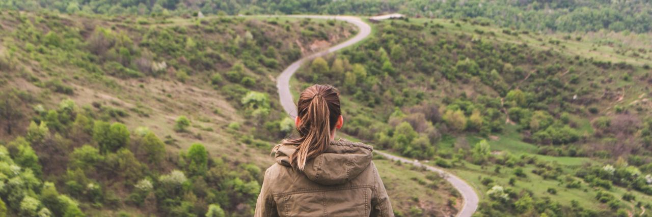 What to Know If You're Starting Therapy for Childhood Sexual Trauma photo of woman sitting on outcrop of rock above valley with winding road stretching out before her