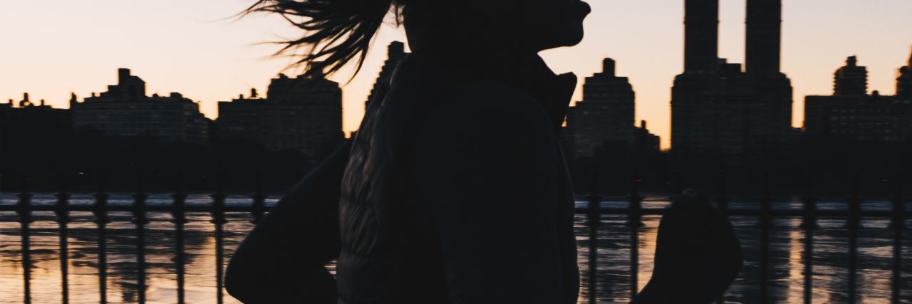 photo of woman silhouetted against sunset and new york skyline running along river
