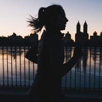 photo of woman silhouetted against sunset and new york skyline running along river