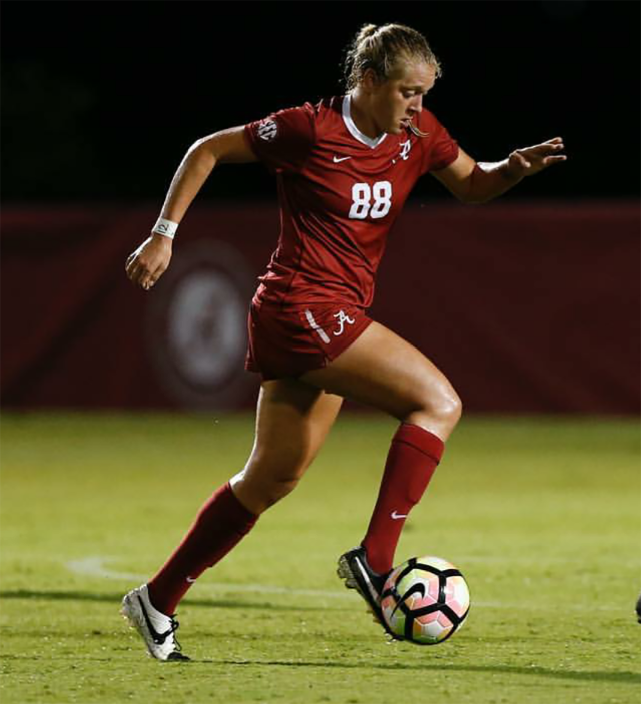 Lacey wearing her University of Alabama uniform, kicking a soccer ball.