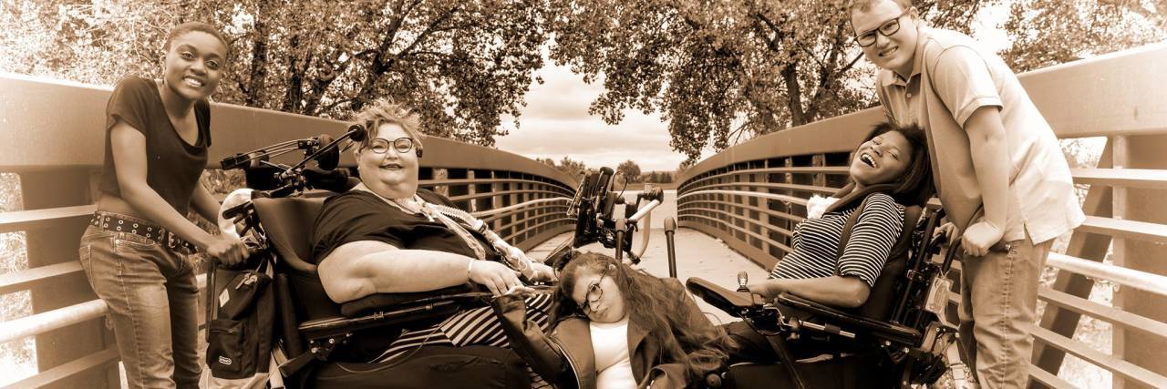 Carrie Ann Lucas with her family. From left to right: Azisa, Carrie, Heather, Adrianne, Anthony. The family is sitting/standing on a bridge, and both Carrie and Adrianne use power wheelchairs.