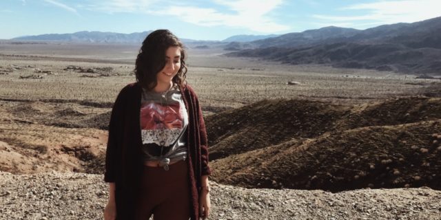 photo of woman posing in front of desert location with mountains and blue sky with clouds