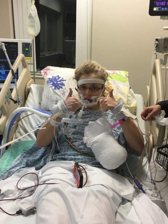 the author in a hospital bed with many wires and tubes connected to her, holding her thumbs up
