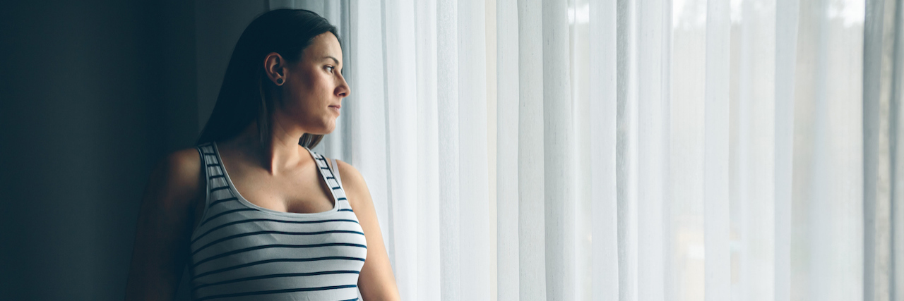 Tips for Recovering After a Cesarean Section (C-Section) A pregnant woman standing by a window covered in white curtains