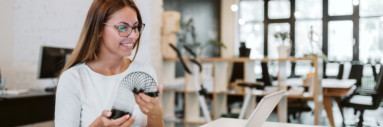 The Small Yet Important Ways My Partner Supports Me Through Anxiety Woman looking at a laptop and holding a slinky