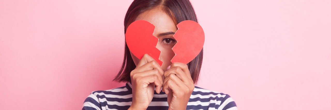 The Reason Dating Is Hard When You're Chronically Ill A woman holding up a broken heart, covering her face