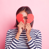 A woman holding up a broken heart, covering her face