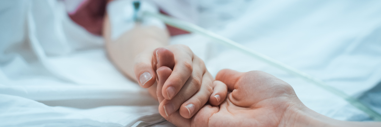 close-up of hand with IV on a hospital bed and another hand holding it