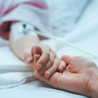 close-up of hand with IV on a hospital bed and another hand holding it
