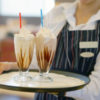the waitress bears two vanilla milkshakes for the client of the hotel restaurant. Two chocolate dairy cocktails on a waitress tray.