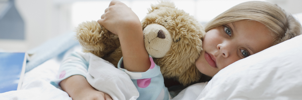 What I Did Not Learn From a Childhood of Chronic Illness a sick girl is laying in a bed hugging a teddy bear