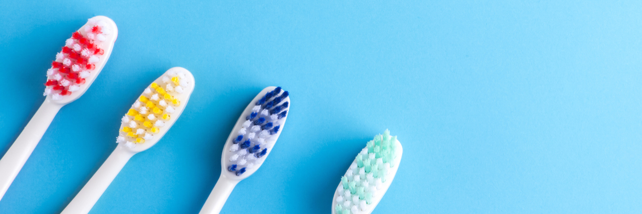 Why Oral Health Is Important for People With Sjögren’s Syndrome Four colorful toothbrushes on blue. Group of y toothbrushes on a blue background.