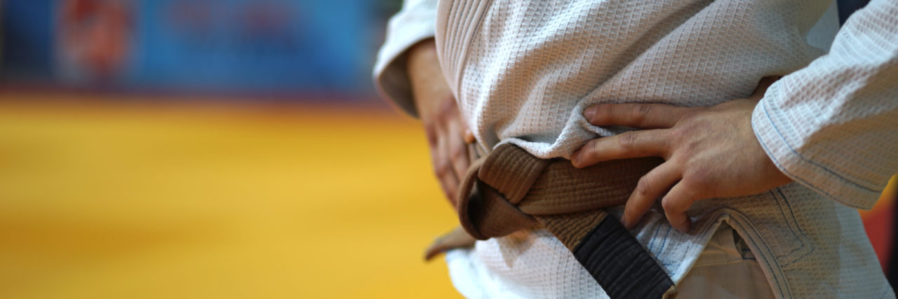 Close up on midsection of a BJJ jiu-jitsu Brazilian jiujitsu Fighter brown belt in a white gi kimono waiting for the fight at the tournament