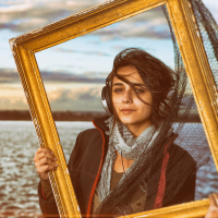 Woman wearing headphones looking through frame, with ocean in the background.