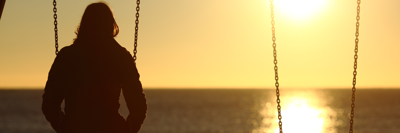 A lonely woman sitting by herself on a swing at sunset at the beach