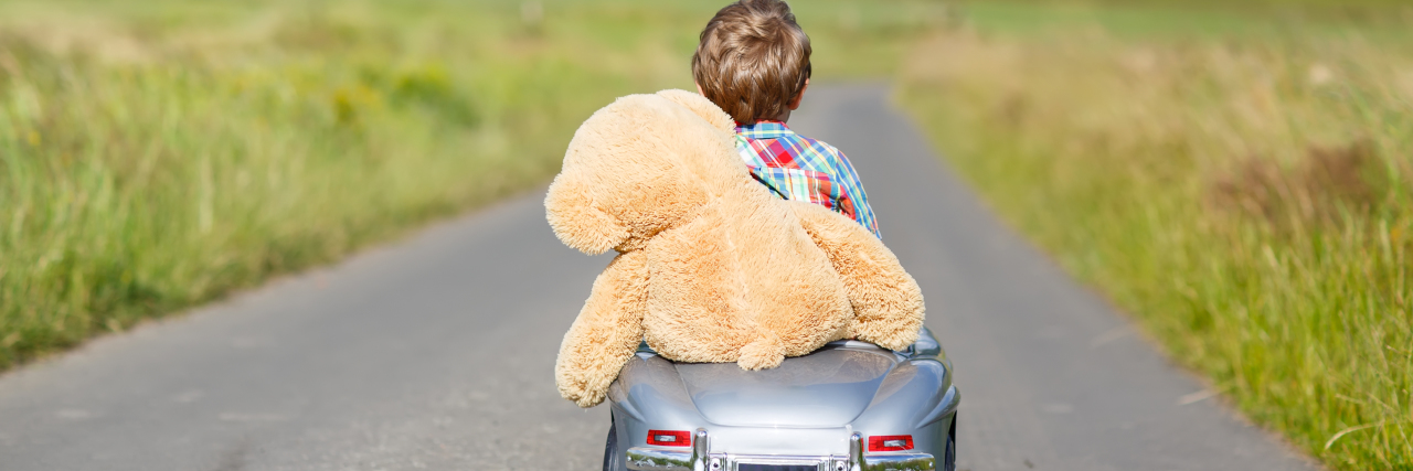 Little boy driving a toy car with a stuffed teddy bear in it