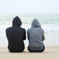 the back view of two people sitting at the beach