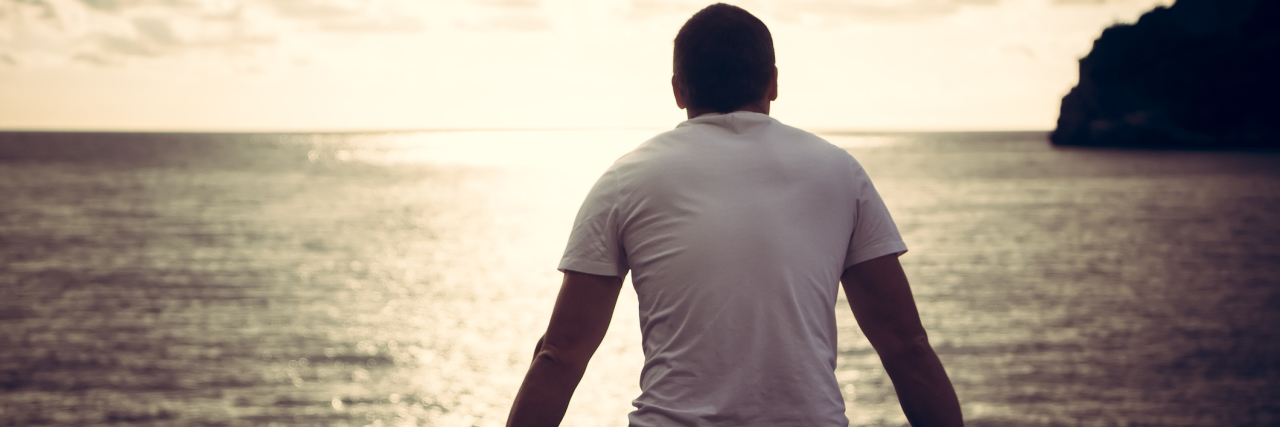 Thalassophobia: Are You Afraid of The Sea? Rear view of lonely man looking with hope at horizon with sunlight during sunset with effect of light at the end of tunnel