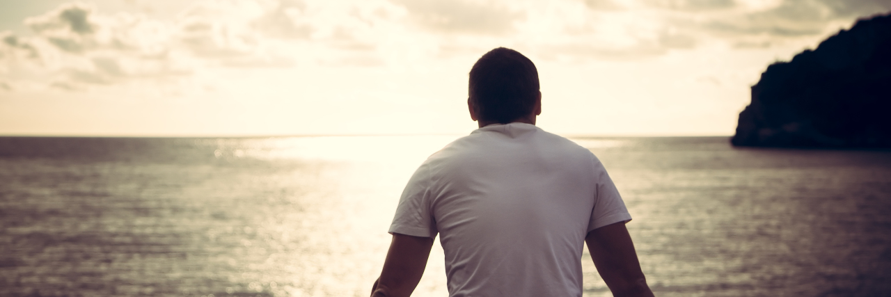 Losing Friendships Because of Chronic Illness Man sitting by the water at sunset.