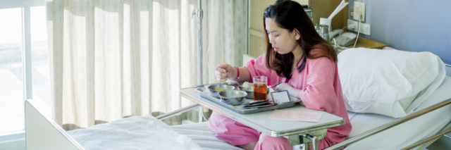 A young woman is eating a meal in a hospital bed.