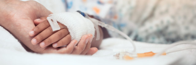 mother holding child's hand in the hospital. child's hand has IV in it.