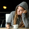 photo of young woman wearing hooded sweater with earphones and phone