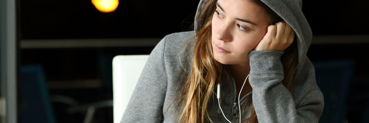 photo of young woman wearing hooded sweater with earphones and phone