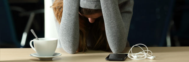 photo of stressed or depressed student wearing hoodie and burying face in arms