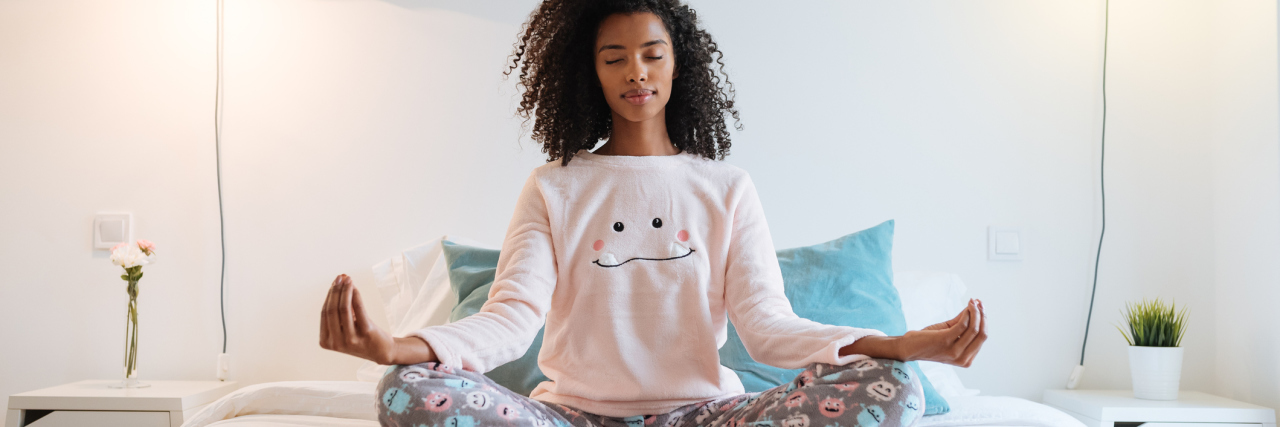 young woman sitting on bed meditating or practicing yoga