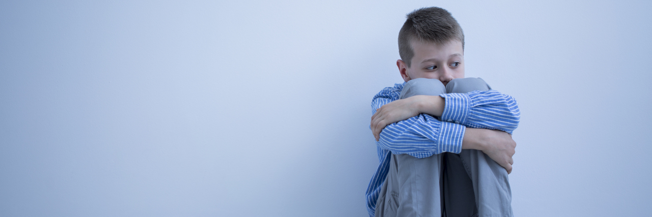 Abuse of Children With Autism Sad boy sitting on the floor with his arms wrapped around his knees.