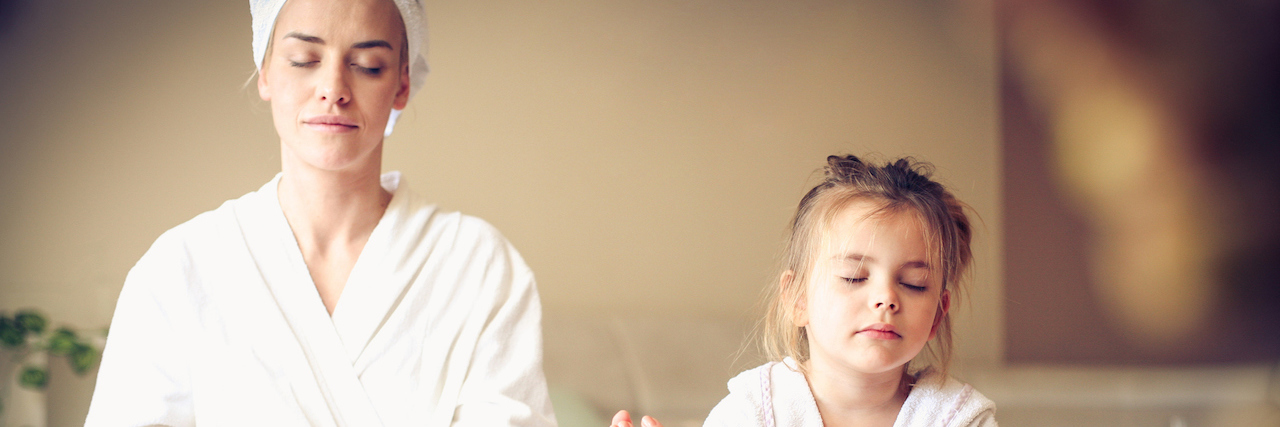 A woman and her daughter in bath robes, sitting cross legged with their eyes closed