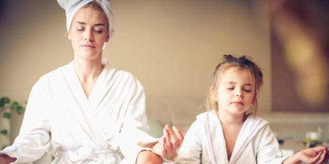 A woman and her daughter in bath robes, sitting cross legged with their eyes closed